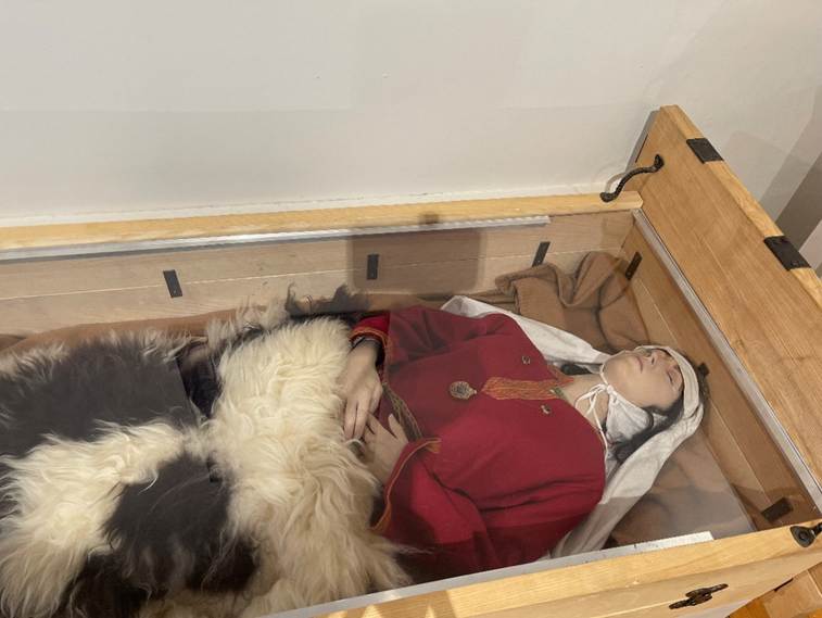 A person lying in a glass case
Description automatically generated